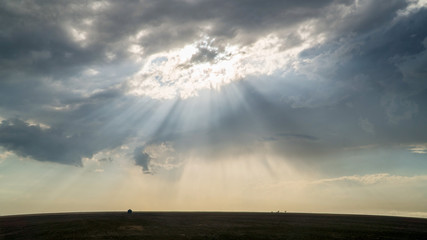 Fototapeta na wymiar Sun rays shining through the clouds moving over flat landscape in the Kansas plains.