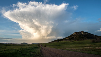 Looking down dirt road towards tall cloud structure during sunset next to Bald Mountain in Colorado.