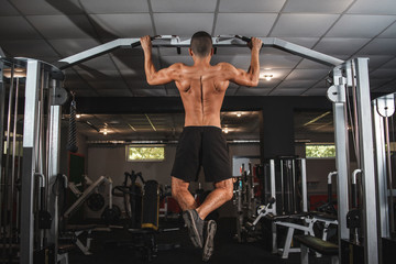 A young athlete trains his back muscles on a horizontal bar with a wide grip. Classes in the gym, healthy lifestyle.