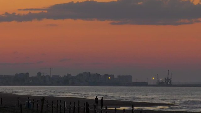 sunset skies over coastal town, people walking on beach