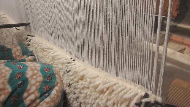 close up on a Moroccan girl weaving a carpet with a manual waving machine, Carpet weaving , Needlework , Morocco .
