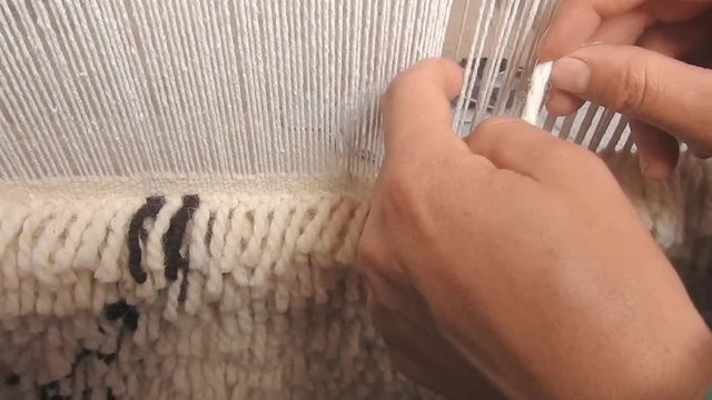 close up on a Moroccan girl weaving a carpet with a manual waving machine, Carpet weaving , Needlework , Morocco .
