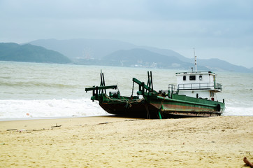 Fishing ship aground on the beach after a storm, Vietnam.Morning on the beach after a storm. Cloudy sky at dawn. The islands are visible on the horizon.