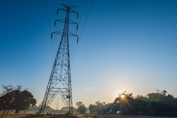 Electric pole and electric cable on the field in the countryside with blue sky.