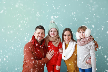 Happy family in winter clothes and falling snow on color background