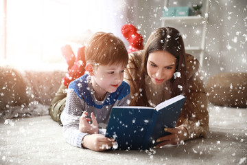 Cute little boy with mother reading book at home on Christmas eve