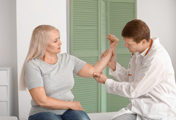 Doctor examining mature woman with joint pain in clinic