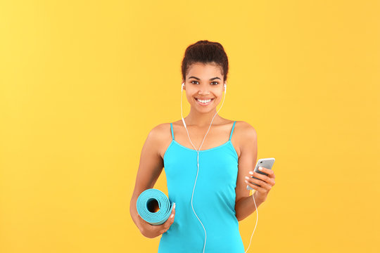 Sporty African-American Woman With Yoga Mat And Mobile Phone On Color Background