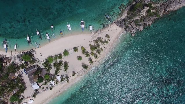 Narrow strip of white sand isthmus beach at sea level between two granite basalt rock outcrops in the middle of the turquoise blue water open ocean in the South Pacific