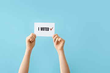 Hands holding paper with text I VOTED on color background