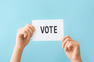 Hands holding paper with text VOTE on color background