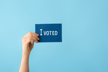 Hand holding paper with text I VOTED on color background