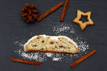 christmas stollen with pine cone, stars  and cinnemon sticks lying on black shale at christmas time