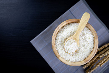 Jasmine rice in wooden bowl and wooden spoon Lay on the cloth and the black wooden table. Top view. Copy space.