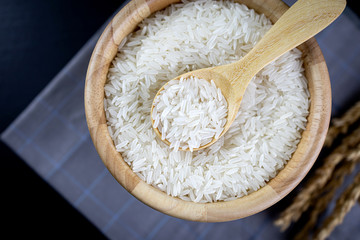 Jasmine rice in wooden bowl and wooden spoon Lay on the cloth and the black wooden table. Close up shot. Top view.