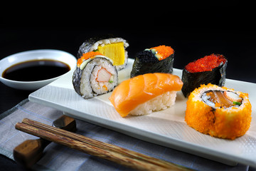Assorted sushi set and Soy sauce on black wooden table background. Space for text. Japanese sushi. 45 degree angle view and close up shot.  Japanese dinner/lunch. Food frame. Different sushi mixed.