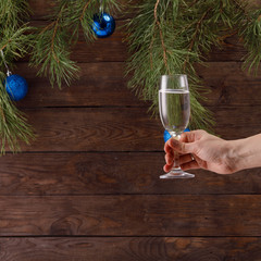 Glass of champagne in hand with bubbles on the background of Christmas decorations. Greeting card. Square.