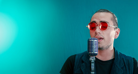 Latin singer man with red glasses and retro microphone on green background with lights