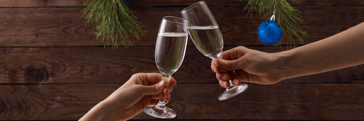 Glasses of champagne with bubbles on the background of Christmas decorations. Two glasses in people's hands touch during a festive toast and sparklers burn beautifully. Beautiful card.