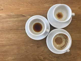 three white cups of finished hot coffee with latte foam left in cups on light brown wooden table with copy space on left side of frame