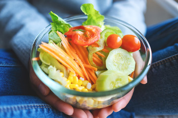 Closeup image of a woman holding a bowl of fresh mixed vegetables salad in hands