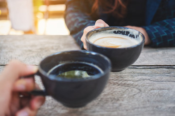 Close up image of two people clinking coffee mugs on wooden table