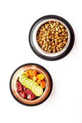 Healthy feed for cats and dogs. Bowls full of dry feed, meat and vegetables on white background top-down
