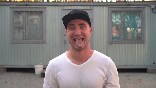 The madman is hiding in a slum from a psychiatric hospital. A psychotic person makes a face. A young man plays a grimace. The guy is fooling around and changing his face.