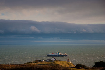 The Baily Lighthouse, Howth. co. Dublin, Baily Lighthouse on Howth cliffs, View of the Baily Lighthouse from the cliff whit cargo ship in background