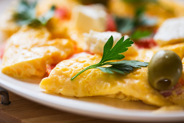 Fluffy french omelette with herbs, olives and feta cheese in a plate.
