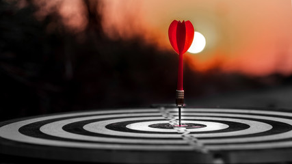 Close up red dart arrow hitting target center dartboard on sunset background. Business targeting...