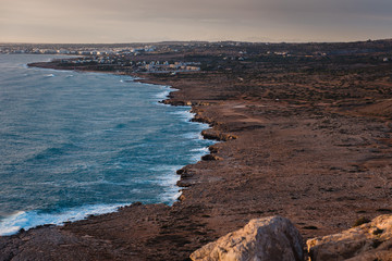 Beautiful landscape. Long rocky shore with restless sea and houses in the background. Cape Greco, Cyprus