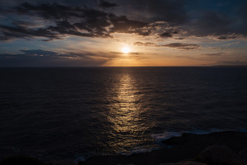 Wonderful sunset. Calm dark sea and golden sky with clouds