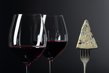 Piece of blue cheese on a fork and red wine.