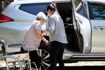 Asian female caregiver helping disabled elderly woman in wheelchair to get into the car,helpful...