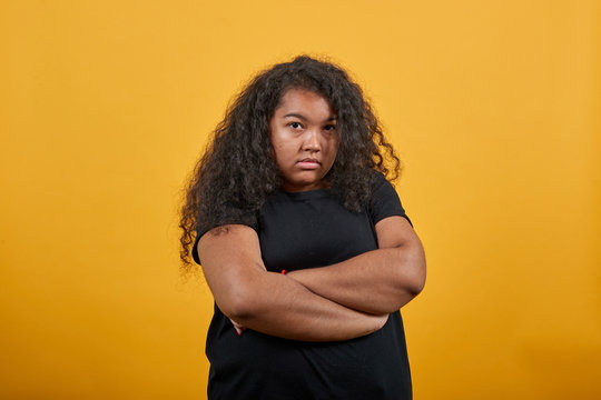 Disappointed young woman with overweight keeping hands crossed, looking at camera over isolated orange background wearing fashion black shirt. People lifestyle concepte.