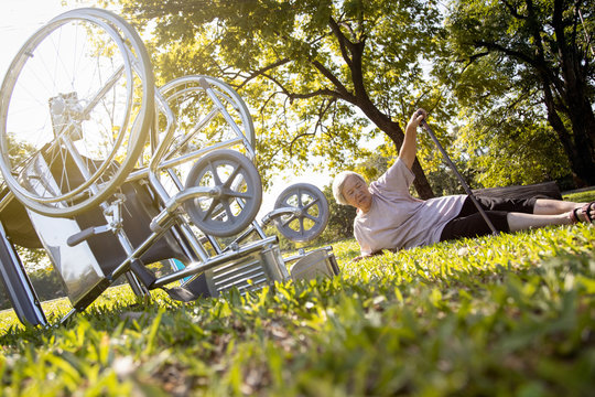 Senior Disabled Woman Falling From Her Wheelchair After An Accident,female Patient With A Leg Pain,asian Elderly Fell On The Grass In The Park Trying To Get Up By Using Walking Stick,accident Concept