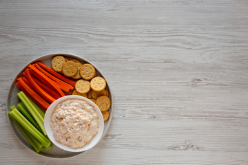 Homemade Pimento Cheese Dip with carrots, celery and crackers over white wooden surface, top view. Flat lay, overhead, from above. Copy space.