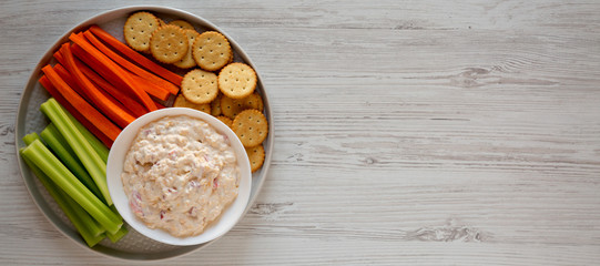 Homemade Pimento Cheese Dip with carrots, celery and crackers over white wooden background, top...