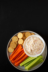 Homemade Pimento Cheese Dip with carrots, celery and crackers over black surface, top view. Flat lay, overhead, from above. Space for text.