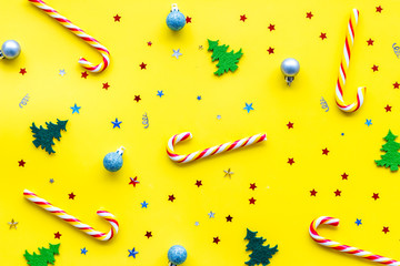 New Year background with Christmas candy cane, festive tree and balls. Pattern on yellow desk top-down