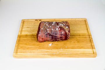 Rolled beef brisket on a wooden chopping board seasoned with sea salt flakes and pepper.