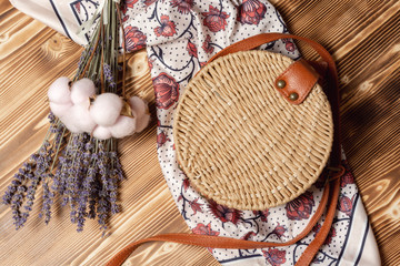 Round straw bag, female silk scarf and bouquet of lavender and cotton flowers. Spring girl fashion outfit 