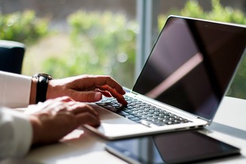 Man typing on laptop in hotel lobby, freelance work concept, close up