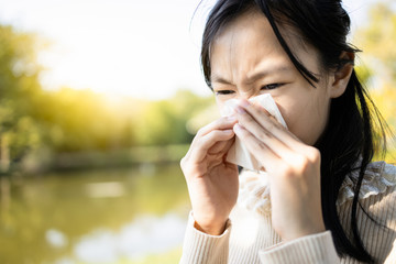 Sick asian child girl sneezing in a tissue blowing her runny nose,hay fever,female teen with blocked nose,weather is changing,suffer from allergic rhinitis woman with allergy in nature outdoor,outside