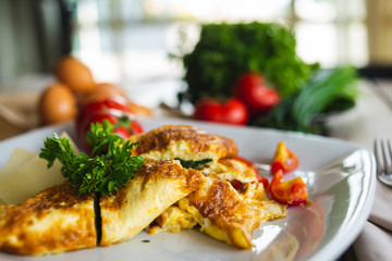 Traditional omelet with vegetables, spinach, tomatoes and herbs on a wooden table in a restaurant.
