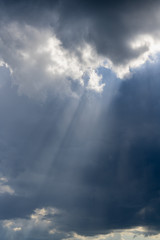 Fototapeta na wymiar Beautiful vertical cloudscape with sun rays shining through the dark clouds