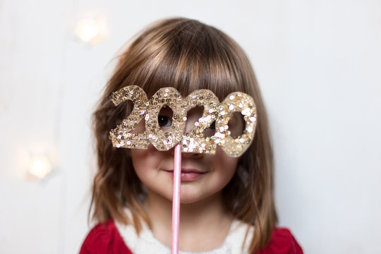 Portrait of a beautiful happy little girl dressed as Santa , holding numbers 2020, isolated on white background.Christmas and New Year. Santa party. Holiday celebration.Selective focus