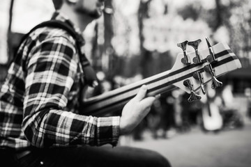 Black and white photo of musician playng on six string fretless bass guitar on the street in front of people.