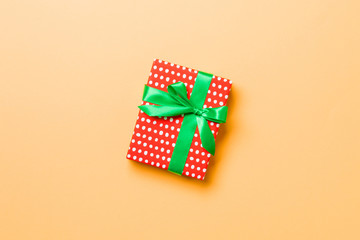 Gift box with green bow for Christmas or New Year day on orange background, top view with copy space